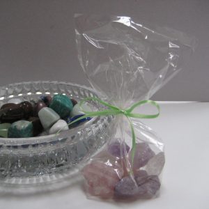 Rosenquarz-Amethyst-Bergkristall: Die einzelnen Edelsteine des Produkts Wasserbelebung mit Edelsteinen - Grundmischung in einem Säckchen, Daneben eine Glasschale mit weiteren Edelsteinen.