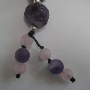 Zoom auf die kleinen Rosenquarz- und Amethyst-Kugeln am Ende des Anhängers einer Edelsteinkette aus Amethyst, Bergkristall und Rosenquarz.