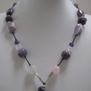 Eine Edelsteinkette aus Amethyst, Bergkristall und Rosenquarz auf einer weißen Damenbüste. Zu sehen ist eine Kette in Lila- und Rosétönen mit einem langen Anhänger.