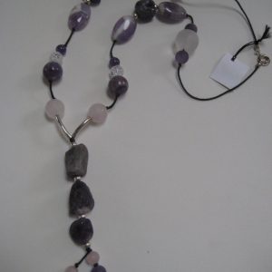 Zoom auf den langen Anhänger aus violetten Amethysten und die Hälfte einer Edelsteinkette aus Amethyst, Bergkristall und Rosenquarz.