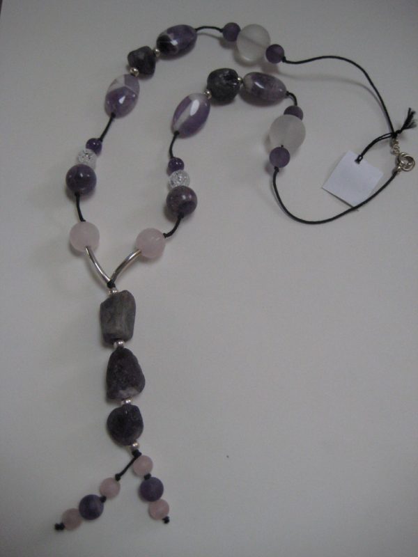 Zoom auf den langen Anhänger aus violetten Amethysten und die Hälfte einer Edelsteinkette aus Amethyst, Bergkristall und Rosenquarz.