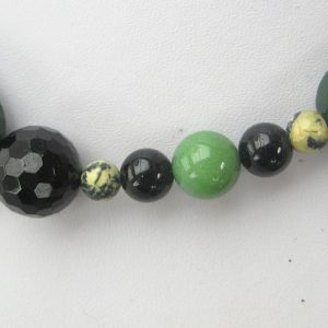 Zoom auf einzelnen helle sowie dunkler grüne und schwarze Steine einer Edelsteinkette aus Jade, Serpentin und Turmalin.