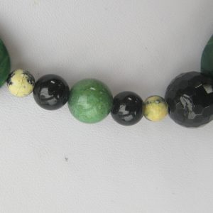 Zoom auf einzelnen helle sowie dunkler grüne und schwarze Steine einer Edelsteinkette aus Jade, Serpentin und Turmalin.