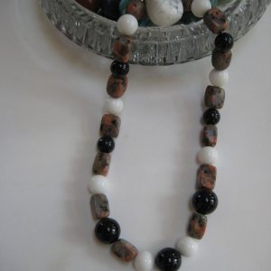 Eine Edelsteinkette aus Turmalin, Jade und Jaspis läuft aus einer Glasschale.