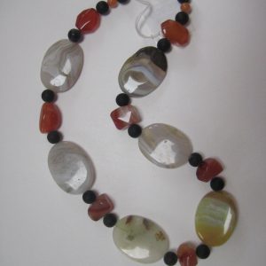Aufgelegte Edelsteinkette aus Onyx, Achat und Karneol. Sie besteht aus Achat-Elipsen in verschiedenen Farbtönen mit Onyxkugeln und orangen Karneolnuggets.