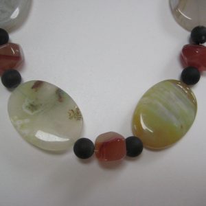 Zoom auf die Achat-Elipsen in verschiedenen Farbtönen, die Onyxkugeln und die orangen Karneolnuggets einer Edelsteinkette aus Onyx, Achat und Karneol.