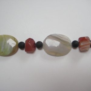 Zoom auf die Achat-Elipsen in verschiedenen Farbtönen, die Onyxkugeln und orangen Karneolnuggets einer Edelsteinkette aus Onyx, Achat und Karneol.