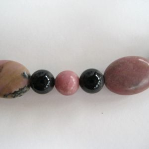 Nahaufnahme von fünf Edelsteinen einer Edelsteinkette aus Onyx und Rhodonit