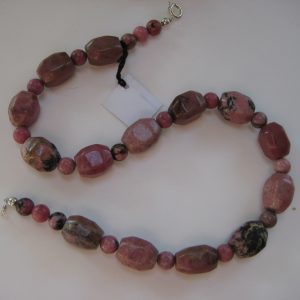 Aufgelegte Edelsteinkette aus Rhodonit. Man sieht große rosefarbene Rhodonit Quader und Kugeln.