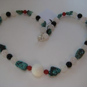 Zu einem Herz gelegte Edelsteinkette aus Türkis, Rosenquarz, Karneol und Onyx auf einer weißen Damenbüste. Die Steine sind türkis, rose, weiß und schwarz.